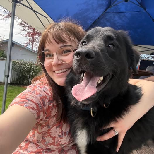 Rach smiling outdoors with her black dog
